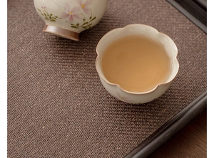 Close-up of ceramic daisy petal teacups with hand-painted pink flowers on a woven tray