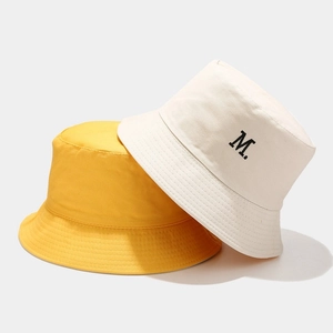 Dettaglio di cappelli a secchiello in cotone giallo e beige con ricamo M e cuciture