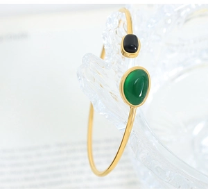 Detail view of a gold open bangle featuring green and black oval gemstones on ice prop