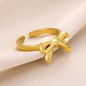 Detailed macro shot of the golden bow-shaped ring on soft beige silk fabric