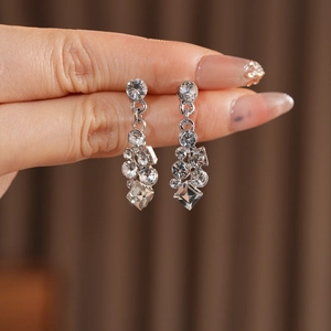 Close-up of silver geometric drop earrings with sparkling rhinestones held by a hand