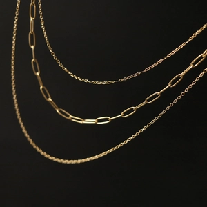Detailed view of layered gold paperclip and classic link chains on a black background