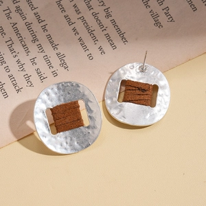 Silver textured round earrings with brown leather wrap on a beige background