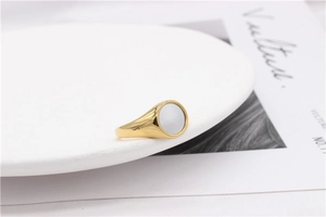 Detailed side view of a gold signet ring featuring a flat white shell inlay on a white stand
