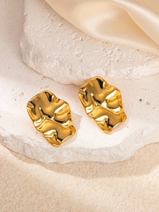 Détail macro de boucles d'oreilles dorées plissées sur pierres blanches et soie champagne