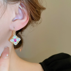 Detail view of gold-plated clover earrings featuring pink gemstone and white enamel petals
