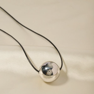 Macro detail of polished steel spherical pendant on a black cord over beige silk fabric