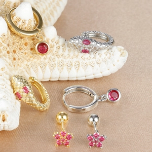 Macro shot of gold and silver snake earrings with rose gemstones on champagne silk