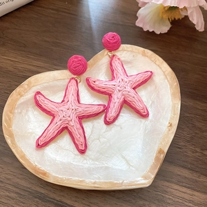 Detail of pink raffia woven starfish earrings on a heart-shaped seashell tray