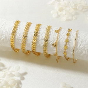 Set di sei bracciali dorati con ciondoli a stella e foglia su elegante trama bianca