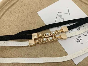 Detail of black and white elastic belts with gold metal buckles and pearl accents