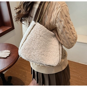 Close-up of cream faux shearling tote bag worn by a model in a warm knit sweater