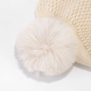 Close-up of fluffy faux fur pom-pom on beige knitted winter hat with soft texture