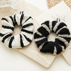 Detail of two black and white striped tweed scrunchies on a natural stone background