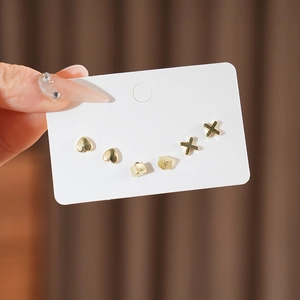 Detailed view of three pairs of minimalist gold heart, square, and X-shaped stud earrings