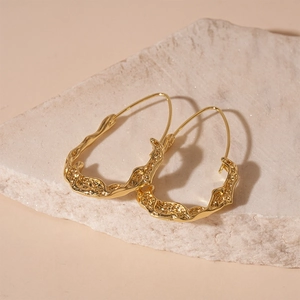 Close-up of golden irregular lava texture C-shape earrings on a natural stone base