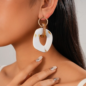 Detail of oversized gold earrings with acrylic white resin and amber textured charms