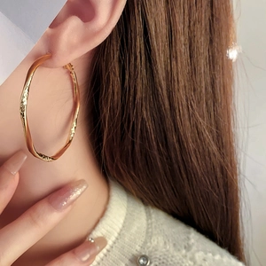 Close-up of a large golden twisted hoop earring worn by a model in a side-view shot