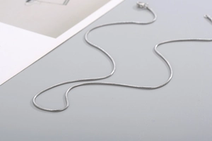 Detailed close-up of a sleek silver stainless steel round snake chain on a gray surface