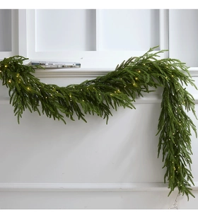 Macro detail of artificial evergreen garland with warm LED lights on white fireplace