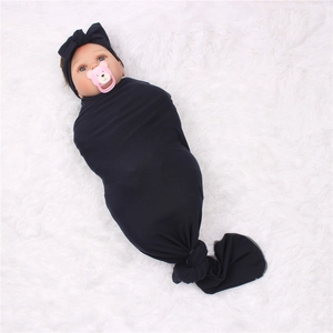 Detail of soft black knotted swaddle wrap and matching bow headband on plush white rug