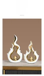 Detail of white ceramic flame sculptures with gold globe on marble surface