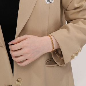 Detailed close-up of a minimalist golden stainless steel cross-link chain on a woman's wrist