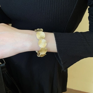 Detail of gold metal disc bracelet with hammered texture on a model's wrist