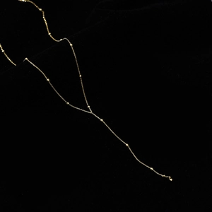 Dettaglio collana lunga a nappa dorata a forma di Y con perline su velluto nero