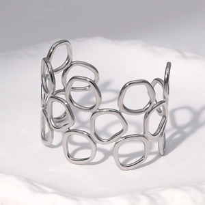 Détail d'un bracelet ajouré géométrique argenté posé sur un plateau en céramique blanche