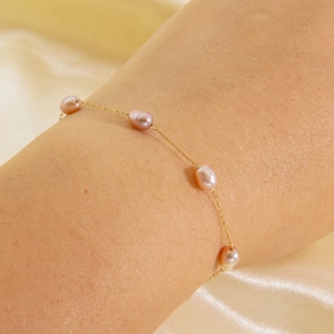 Elegant 14K gold-plated titanium bracelet with pink oval pearls on a soft silk background