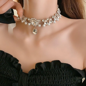 Detail view of flower-shaped rhinestone necklace with teardrop pearl on female model