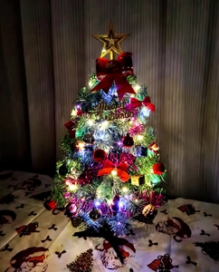 Detailed view of mini Christmas tree featuring LED lights, red bows, and gold star topper