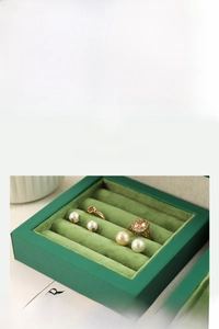 Macro detail of dark green velvet jewelry tray featuring slots for rings and pearl earrings