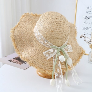 Detail of handwoven straw hat featuring white lace ribbons and tulip pendants