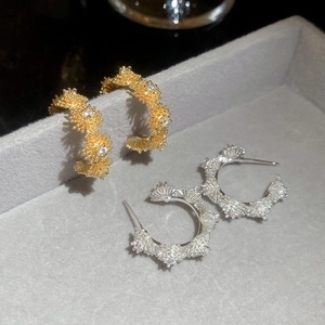 Detail view of C-shaped zircon flower earrings in gold and silver on a velvet tray