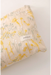 Détail de la broderie florale et de la texture sur une trousse à maquillage en lin beige