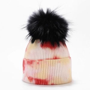 Detailed view of the red and yellow tie-dye knit beanie with a large black faux fur pom-pom
