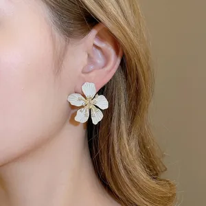 Elegant matte white floral stud earrings with tiny diamonds shown on female model