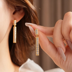 Détail de longues boucles d'oreilles à pompons dorés avec zircons portées par un mannequin