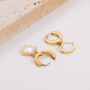 Elegant gold earrings with white four-petal flower charms on white background