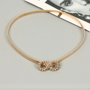 Macro view of elastic gold metal waist chain with textured figure-eight infinity buckle