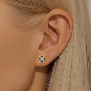 Macro detail of a gold sun stud earring featuring a vibrant turquoise center stone