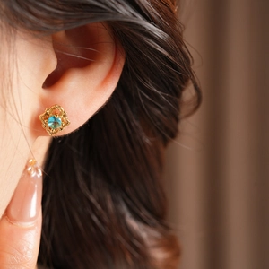 Close-up of vintage flower shaped gold earring with a teal gemstone worn on the ear