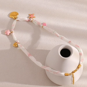 Floral fabric necklace with gold seashell and pink starfish pendants on white vase