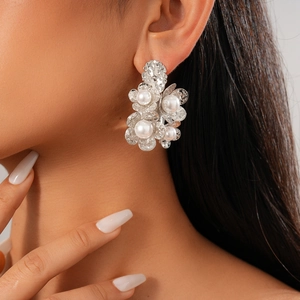Detail of silver flower earrings with pearls worn by a model on a clean gradient background