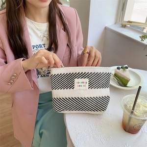 Detail of black and white striped cosmetic bag with a small woven texture and a brand label
