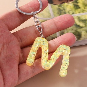 Detail of letter M keychain made of clear resin with yellow and green iridescent sequins