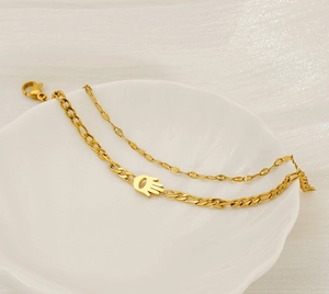 Detailed shot of double-layered gold Hamsa hand bracelet on a ceramic jewelry tray