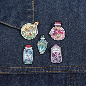 Detail of five mushroom potion bottle enamel pins displayed on dark blue denim fabric